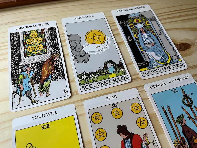 May include: Tarot card spread with ten cards, including the Ace of Pentacles, The High Priestess, and the Eight of Wands. The cards are laid out on a wooden surface. The cards have titles such as "Touch Love", "Emotional Space", "Gentle Influence", "Your Will", "Fear", and "Seemingly Impossible".