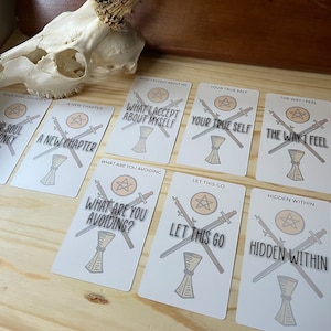 May include: A set of ten tarot cards with white backgrounds and black text. Each card features a pentacle, two swords, and a phrase. The phrases include "Your Soul Journey", "A New Chapter", "What I Accept About Myself", "Your True Self", "The Way I Feel", "What Are You Avoiding", "Let This Go", "Hidden Within", and more.