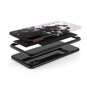 May include: A black phone case with a white and brown cowhide pattern. The case is shown in three layers, revealing the phone case, a black protective layer, and the phone itself.