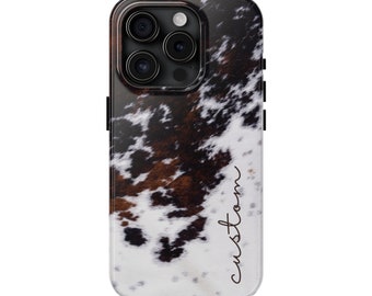 May include: A black phone case with a white and brown cowhide pattern. The case has a raised camera bump and the word "custom" is written on the side.