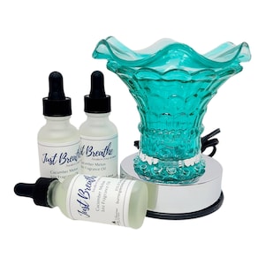 May include: A teal glass essential oil diffuser with a silver base and three small bottles of Cucumber Melon fragrance oil. The bottles have black droppers and the text "Just Breathe" is visible on the labels. The diffuser has a flower-like design.