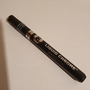 Pode incluir: Marcador preto com letras douradas que dizem "Liquid Chrome™ Mirror Effect".
