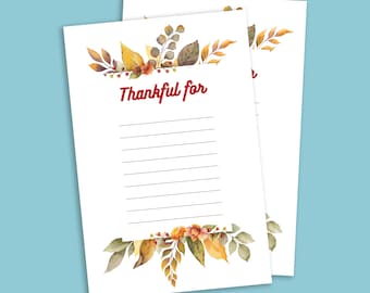 Puede incluir: Dos hojas de papel blancas con las palabras "Thankful for" en escritura roja. La parte superior e inferior de las páginas están decoradas con ilustraciones de acuarela de hojas de otoño en tonos de amarillo, naranja y marrón. Rayado para escribir.