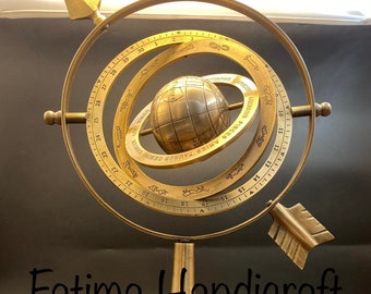 Może przedstawiać: Złoty metalowy globus niebieski z pierścieniem znaków zodiaku i strzałką kompasu. Globus stoi na podstawie z okrągłą podstawą. Tekst na globusie brzmi "AQUARIUS PISCES ARIES TAURUS GEMINI CANCER LEO VIRGO LIBRA SCORPIO SAGITTARIUS CAPRICORN AQUARIUS".
