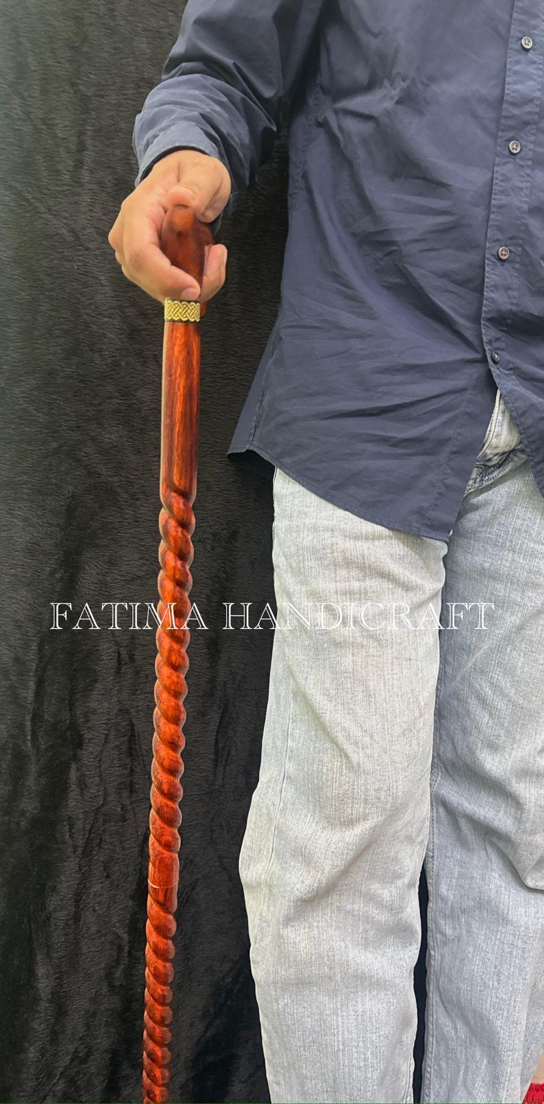 Op de afbeelding: Een houten wandelstok met een gedraaid ontwerp. De stok is diep roodbruin van kleur, met een goudkleurige band aan de bovenkant. De tekst "FATIMA HANDICRAFT" is zichtbaar op de afbeelding.