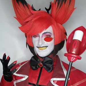 Puede incluir: Una persona con un disfraz rojo y negro con cuernos y una pajarita. Está sosteniendo un bastón rojo y negro con una botella blanca en la parte superior. La persona tiene el pelo rojo y los ojos rojos.