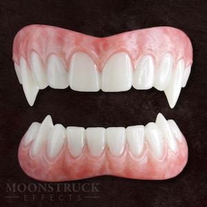 May include: A set of two vampire teeth prosthetics. The upper and lower sets are made of white teeth set in a pink gum base. The teeth are sharp and pointed, with the brand name "MOONSTRUCK EFFECTS" at the bottom.