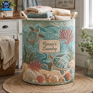 May include: A cylindrical fabric laundry hamper featuring a quilted ocean theme with sea turtles, coral, and seashells in shades of blue, green, and tan. A central rectangular patch displays the embroidered text "Nonna's Laundry" in script.