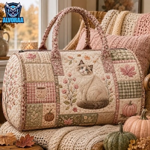 May include: A quilted duffel bag featuring a patchwork design with a central cat illustration, floral motifs, pumpkins, and a coffee mug. The bag has two fabric handles and a beige, pink, and green color palette with autumn-themed patterns.