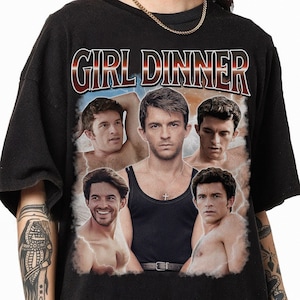 May include: Black t-shirt with the text "GIRL DINNER" in a red and white font. The shirt features a collage of five men in various poses, some shirtless, with a blue and white cloudy background.