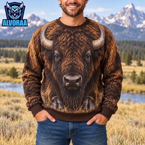 May include: A brown long-sleeve sweatshirt featuring a large, detailed graphic of a bison head with prominent horns and textured fur. The design covers the front of the garment, which has a crew neckline and solid brown ribbed cuffs and hem.