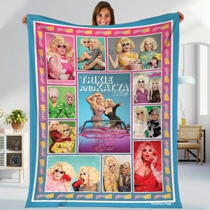 May include: A large, rectangular blanket with a collage of images featuring Trixie and Katya. The blanket has a light blue border and a pink and white border with the words "Trixie & Katya" repeated. The central image has the text "Trixie and Katya Live".