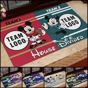 May include: A rectangular doormat featuring Mickey and Minnie Mouse in football attire. The mat is divided into two sections, red and teal, with the text "TEAM 1" and "TEAM 2". Each section has a circle for a team logo and the words "House Divided".