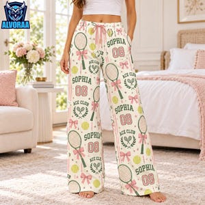 May include: High-waisted lounge pants featuring a white base with a repeating pattern of tennis rackets, pink bows, yellow tennis balls, and the text "SOPHIA 08 ACE CLUB" in green and pink. The pants have a drawstring waist and wide legs.
