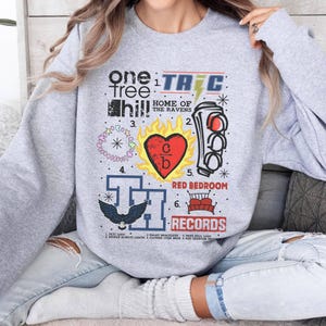 May include: Gray sweatshirt with a graphic design featuring the text "One Tree Hill" and various other designs, including a heart, a stoplight, and a crown. The text "TRIC RECORDS" is also included.
