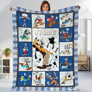 May include: A blue and white fleece blanket with a patchwork design featuring various cartoon characters playing sports. The characters include Goofy, Mickey Mouse, and Donald Duck. The blanket has the word "NAME" in the center.