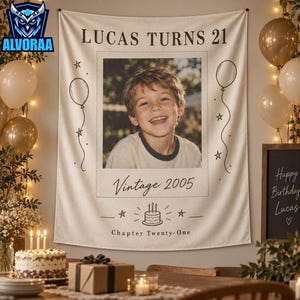 May include: A cream-colored fabric wall hanging featuring the text LUCAS TURNS 21 at the top, a central photograph of a young person, the text Vintage 2005, a graphic of a birthday cake, and the text Chapter Twenty-One, decorated with line-art balloons.