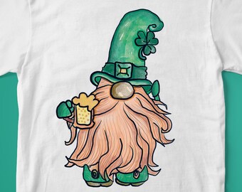 Puede incluir: Camiseta blanca con un gnomo verde y naranja sosteniendo una jarra de cerveza. El gnomo lleva un sombrero verde con un trébol.