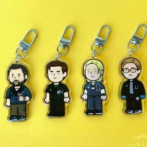 May include: Four cartoon keychains featuring medical professionals, each with a silver clasp. The characters are dressed in scrubs and jackets, with varying hairstyles and accessories. The background is a solid yellow.