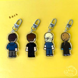 May include: Four acrylic keychains with silver-colored hardware. Each keychain features a cartoon figure with different hairstyles and outfits. The figures are shown from the back. The background is yellow with the word "Back" in the upper left corner.
