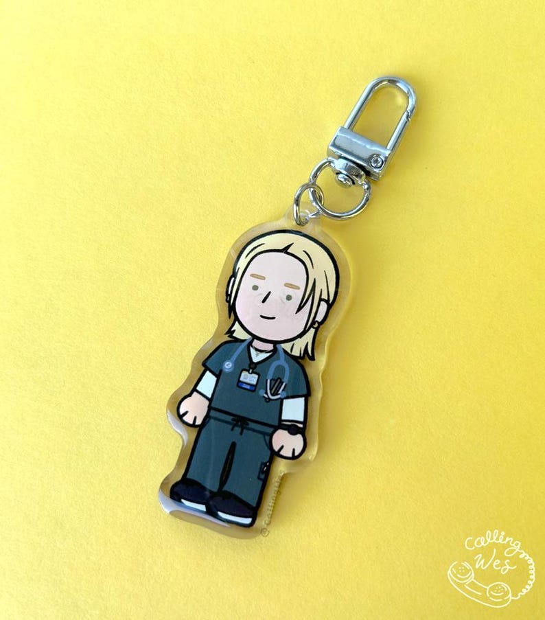 May include: A clear acrylic keychain featuring a cartoon illustration of a healthcare worker in teal scrubs, a stethoscope, and a name tag. The keychain has a silver clasp and a small ring. The background is a solid yellow.