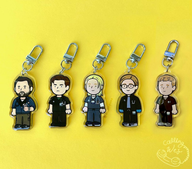 May include: Five acrylic keychains featuring cartoon illustrations of medical professionals. Each keychain has a silver clasp and depicts a different character in scrubs and a lab coat. The background is a solid yellow.