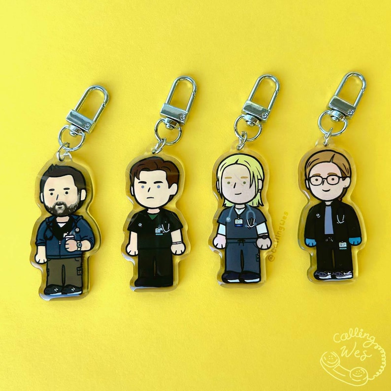 May include: Four cartoon keychains featuring medical professionals, each with a silver clasp. The characters are dressed in scrubs and jackets, with varying hairstyles and accessories. The background is a solid yellow.