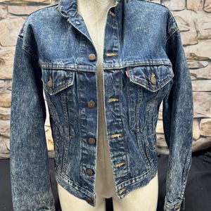 May include: A blue denim jacket with a faded look. The jacket has a button closure, two front pockets, and a single chest pocket.