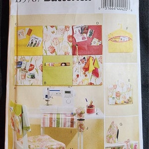 May include: A sewing pattern by Butterick, B5767, featuring various sewing projects. The image shows a sewing machine, chair, and table with fabric accessories. The pattern includes instructions for making organizers and storage solutions.