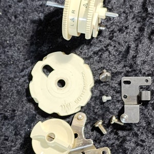 May include: A set of vintage sewing machine parts, including a white plastic knob with the text "BOBBIN" and a white plastic dial with the text "L & R" and numbers 1-2-3-4-5.