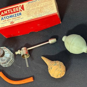 May include: An antique Kantleek Atomizer set with a red and white box, glass bottle, metal sprayer, rubber bulb, and orange rubber tube. The box reads "KANTLEEK ATOMIZER with glass liquid-tube". The set is likely from the early to mid-20th century.