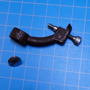 May include: A brown metal bracket with two silver screws and a separate silver screw. The bracket has a curved shape and a circular opening at one end.