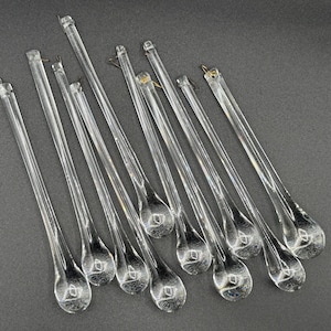 Può includere: Una collezione di ornamenti trasparenti a forma di goccia in vetro con ganci in metallo per appenderli. Gli ornamenti sono disposti su una superficie grigio scuro, mostrando le loro qualità trasparenti e riflettenti. Ideali per le decorazioni natalizie o per la casa.