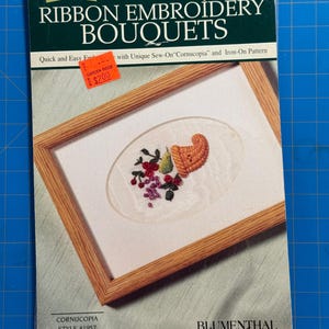 May include: A vintage ribbon embroidery kit featuring a framed design of a cornucopia with flowers and fruit. The kit includes the text "RIBBON EMBROIDERY BOUQUETS" and "CORNUCOPIA STYLE #1957". The price tag shows $2.00.