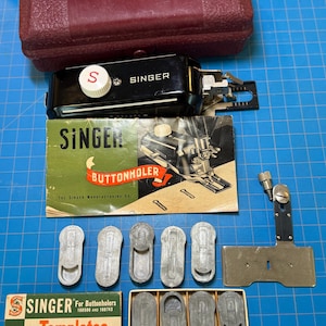 May include: A collection of Singer sewing machine attachments and accessories. Includes a red case, a black buttonholer, a green and yellow buttonholer manual, templates, and various metal components. The Singer logo is visible on several items.