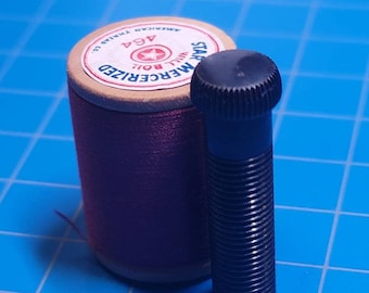 May include: A spool of pink thread with a white label that reads "STAR MERCERIZED WILL BOIL 464 AMERICAN THREAD CO.". A black plastic screw with a hexagonal head is next to the spool.