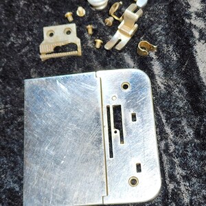 May include: A silver sewing machine foot, a silver sewing machine needle plate, a silver sewing machine presser foot, a silver sewing machine bobbin winder, and a silver sewing machine needle plate screw.