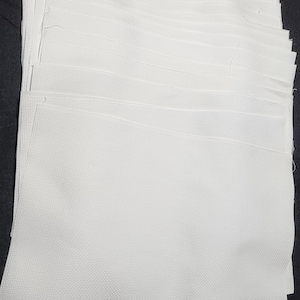 May include: A stack of white Aida cloth, a type of fabric used for cross-stitch embroidery.