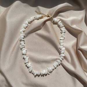 Könnte beinhalten: Eine Halskette aus weißen Steinen mit goldenen Akzenten. Die Halskette besteht aus kleinen, unregelmäßig geformten Steinen und ist auf einer goldenen Kette aufgefädelt.