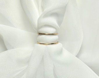 Puede incluir: Dos anillos finos de oro apilados uno encima del otro. Los anillos son lisos y tienen una textura ligeramente martillada.
