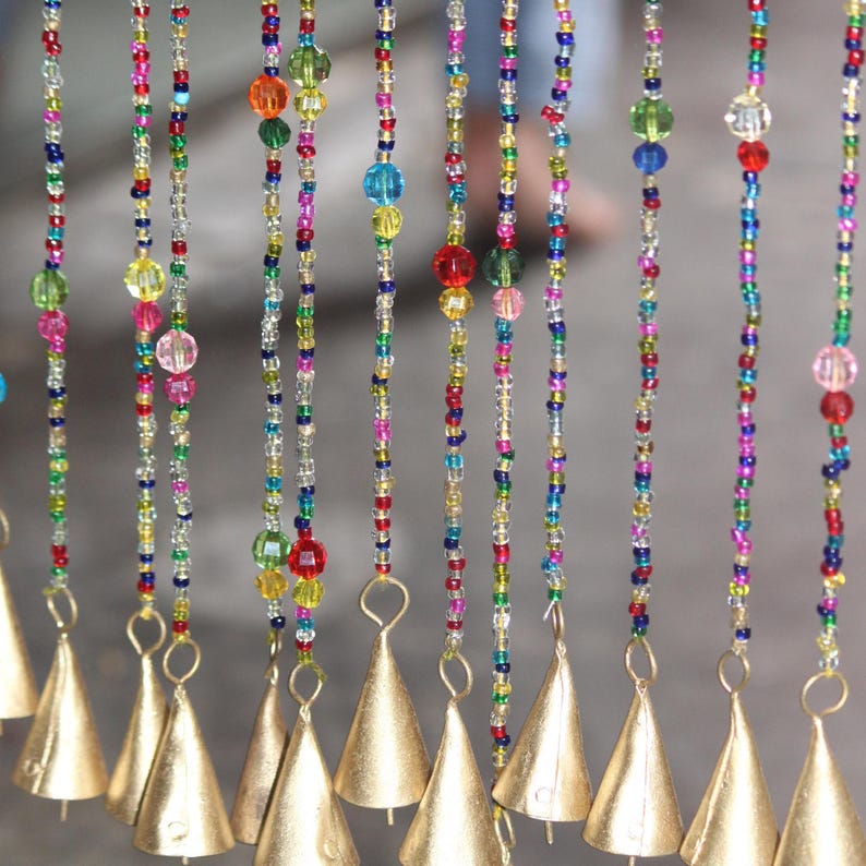May include: A colourful beaded curtain with gold bells hanging from the bottom. The beads are in various colours, including red, blue, green, and yellow.