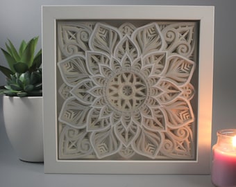 May include: A white framed square wall art piece with a 3D paper cut-out design of a mandala in shades of beige and white.