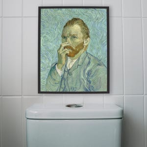 May include: A framed print of a self-portrait by Vincent van Gogh, featuring the artist in a blue suit, with a red beard and hair. The artwork is displayed above a white toilet in a tiled bathroom.