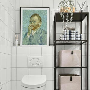 May include: A framed print of Vincent van Gogh's self-portrait hangs above a white toilet. A black metal shelf holds towels and storage bins. The bathroom features white tile walls and a modern design.