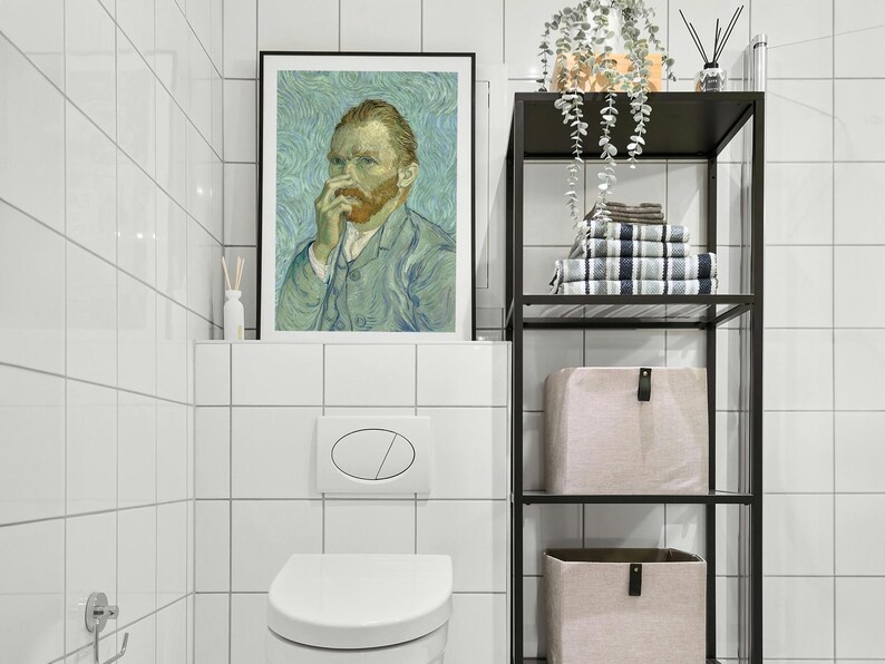 May include: A framed print of Vincent van Gogh's self-portrait hangs above a white toilet. A black metal shelf holds towels and storage bins. The bathroom features white tile walls and a modern design.