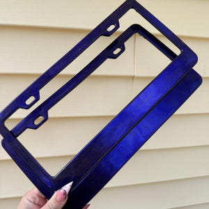 May include: Two blue license plate frames with a glittery finish. The frames are stacked on top of each other.