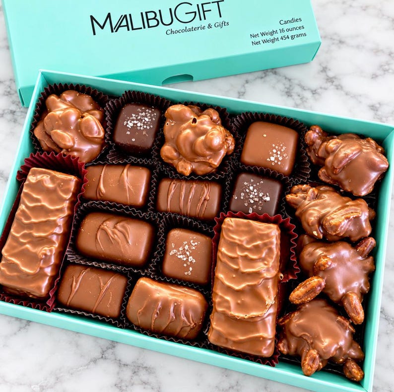 Op de afbeelding: Een turquoise doos gevuld met een assortiment melk- en pure chocolaatjes, waaronder notenclusters, vierkantjes met zeezout en rechthoekige repen. Het deksel is gelabeld met MALIBUGIFT Chocolaterie & Gifts en een nettogewicht van 454 gram.