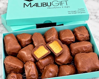 May include: A turquoise gift box labeled MALIBU GIFT Chocolaterie & Gifts containing milk chocolate-covered honeycomb candies. The box lid displays the text Net Weight 16 ounces. One piece of candy is split in half to reveal a golden honeycomb center.