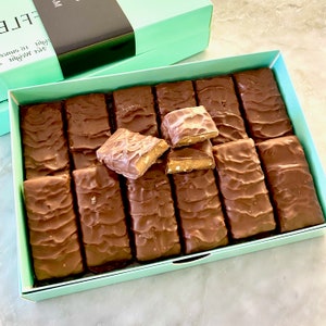 May include: A mint green box filled with chocolate covered toffee bars. The box is open and some of the bars are broken, revealing the toffee inside.