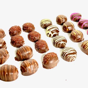 May include: An assortment of chocolate truffles on a white surface. Some truffles are decorated with chocolate drizzle, sprinkles, or colored icing. The truffles are various shapes and sizes, offering a visually appealing display of confectionery treats.